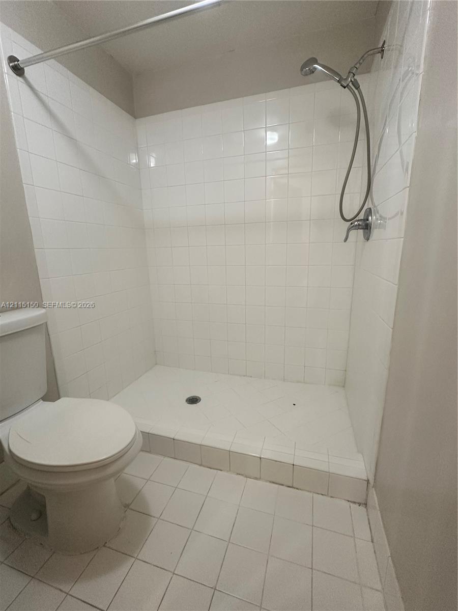 Walk-in shower enclosure featuring white wall tiling, a raised tiled threshold, and a chrome handheld shower fixture, accompanied by a white porcelain toilet