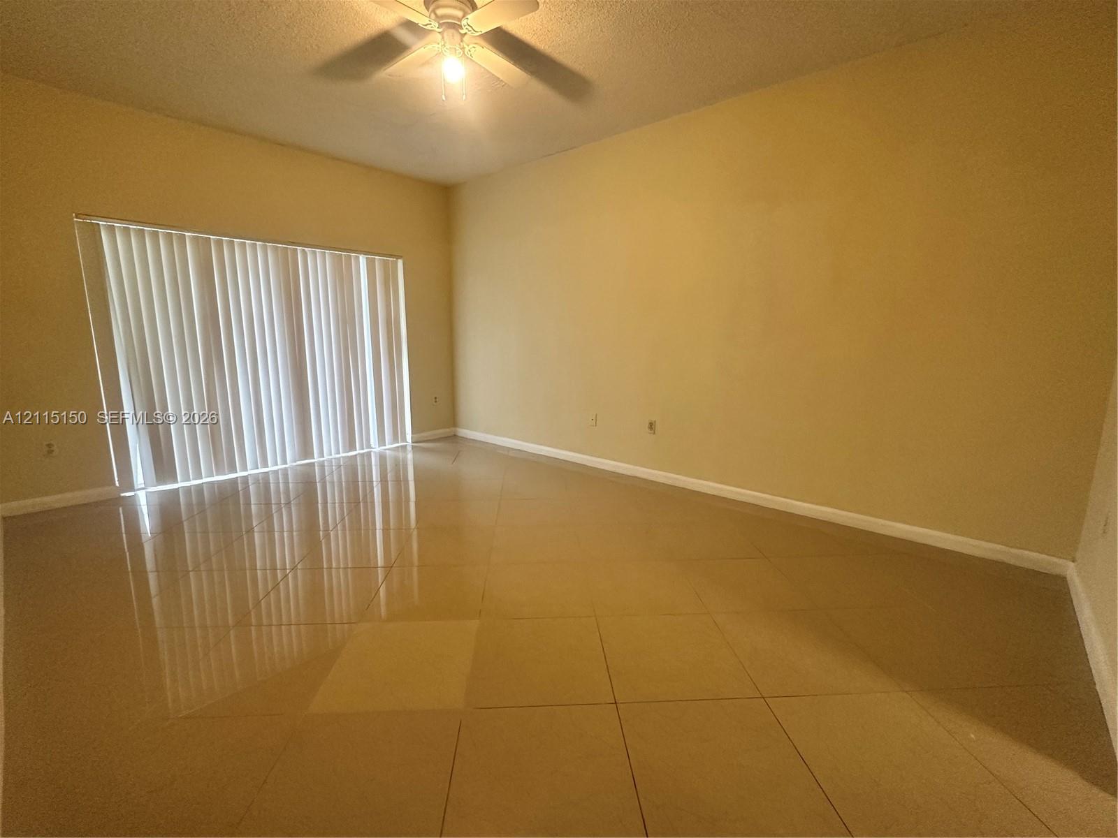 Neutral-toned tile flooring, tall ceilings, and floor-to-ceiling vertical blinds covering a large sliding glass door