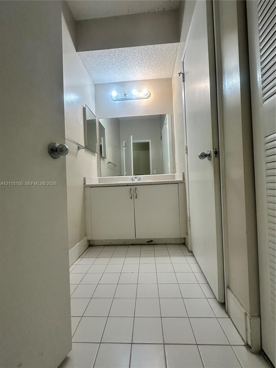 Bathroom vanity featuring a white cabinet base, integrated countertop, and mounted light fixture, complemented by tiled flooring