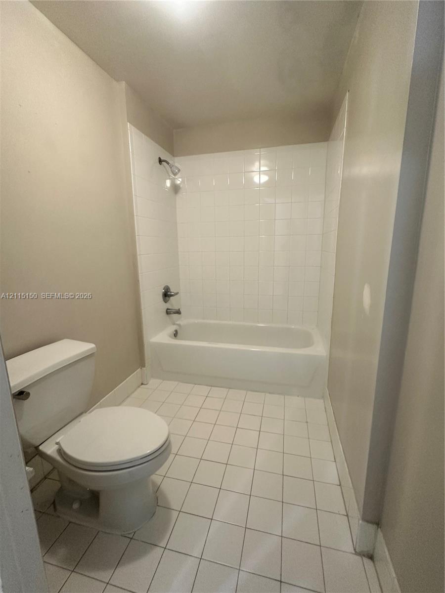 Bathroom featuring a white ceramic tile floor, bathtub with a white tile surround, wall-mounted shower head, and dual-handle plumbing fixture