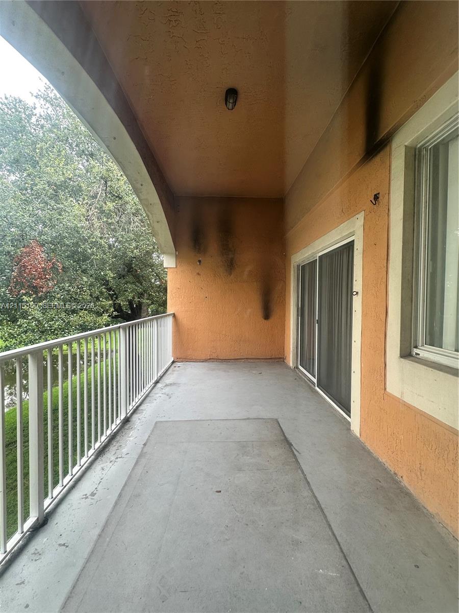 Covered balcony featuring a white metal railing, concrete flooring, sliding glass door, and a recessed ceiling light fixture
