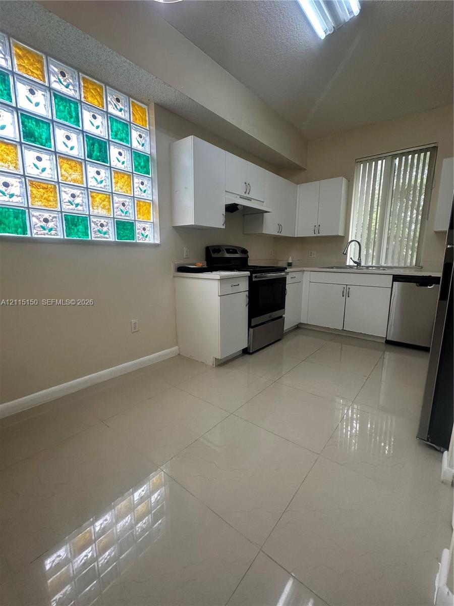Kitchen featuring white cabinetry, large-format tile flooring, stainless steel appliances, and a glass block window with multicolor accents