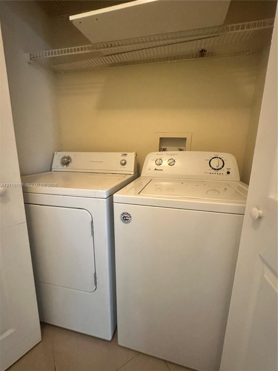 Laundry closet featuring white top-load washer and dryer, built-in wire shelving, and neutral wall finish
