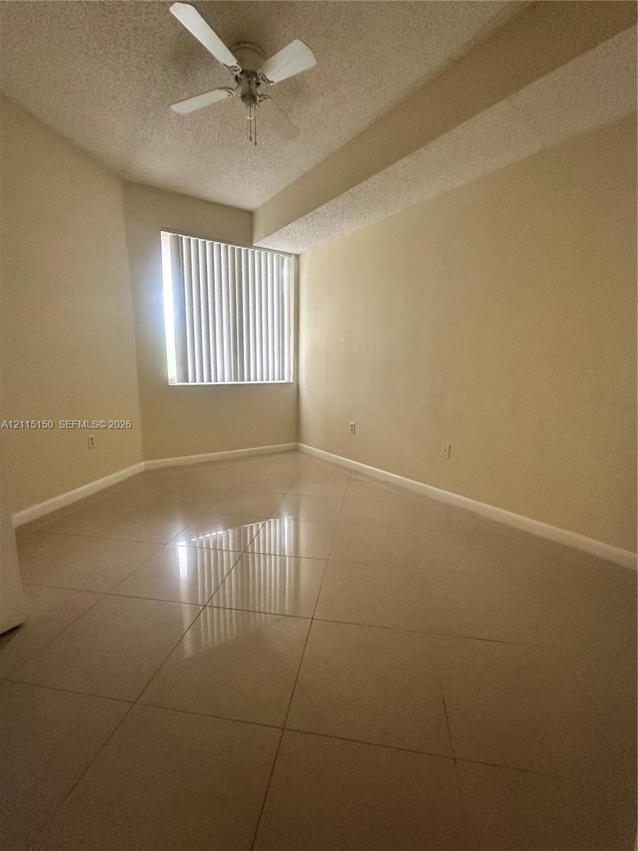 Interior room featuring large-format tile flooring, a neutral color palette, a ceiling fan with integrated lighting, and vertical window blinds