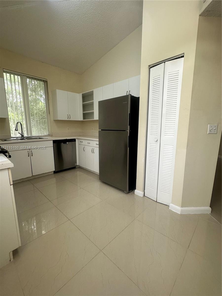 Kitchen featuring white cabinetry, stainless steel appliances, tile flooring, louvered closet doors, and a high ceiling