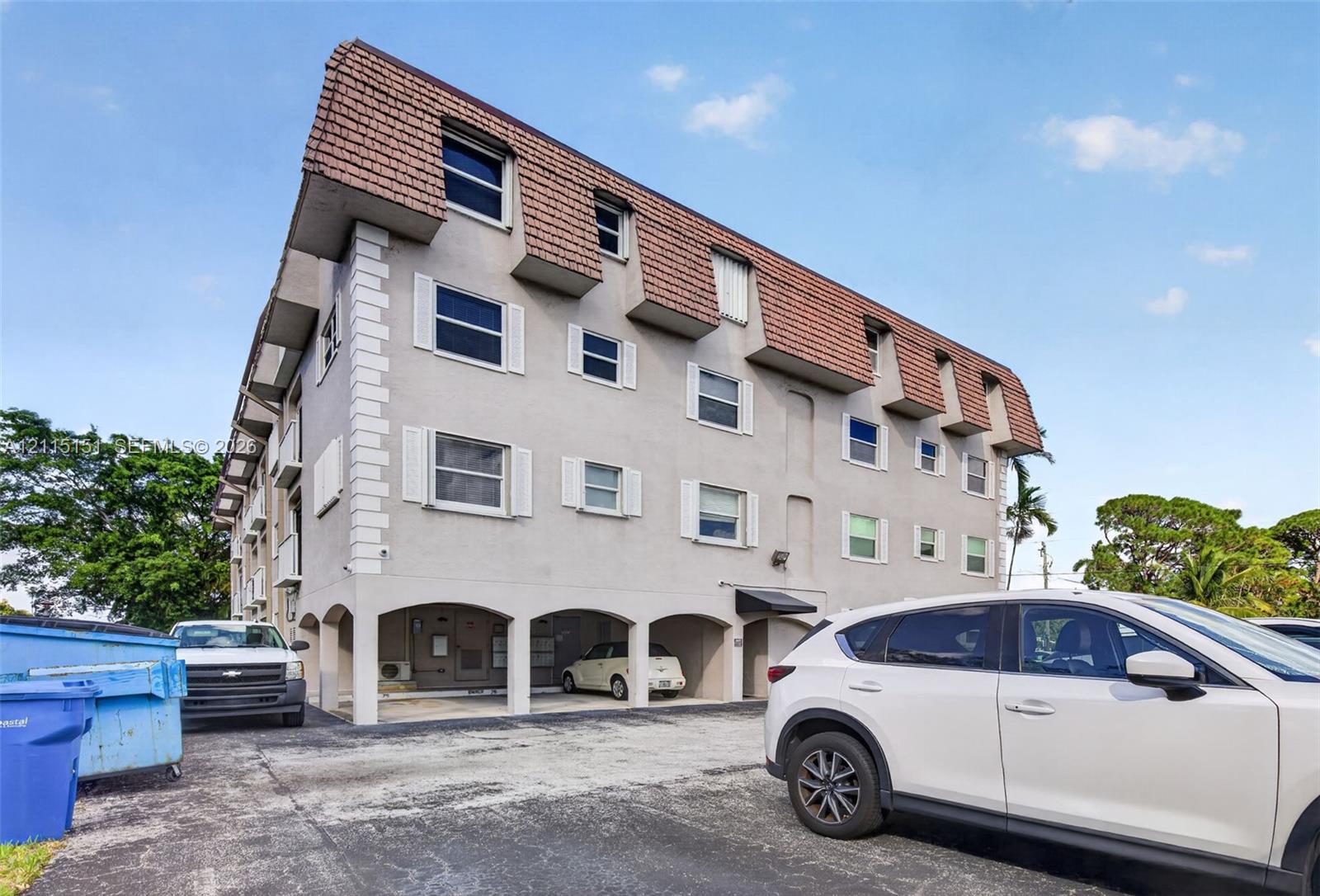 Multi-story exterior featuring a mansard roof, stucco facade, decorative window shutters, and covered ground-level parking Multi-story exterior featuring a mansard roof, stucco facade, decorative window shutters, and covered ground-level parking