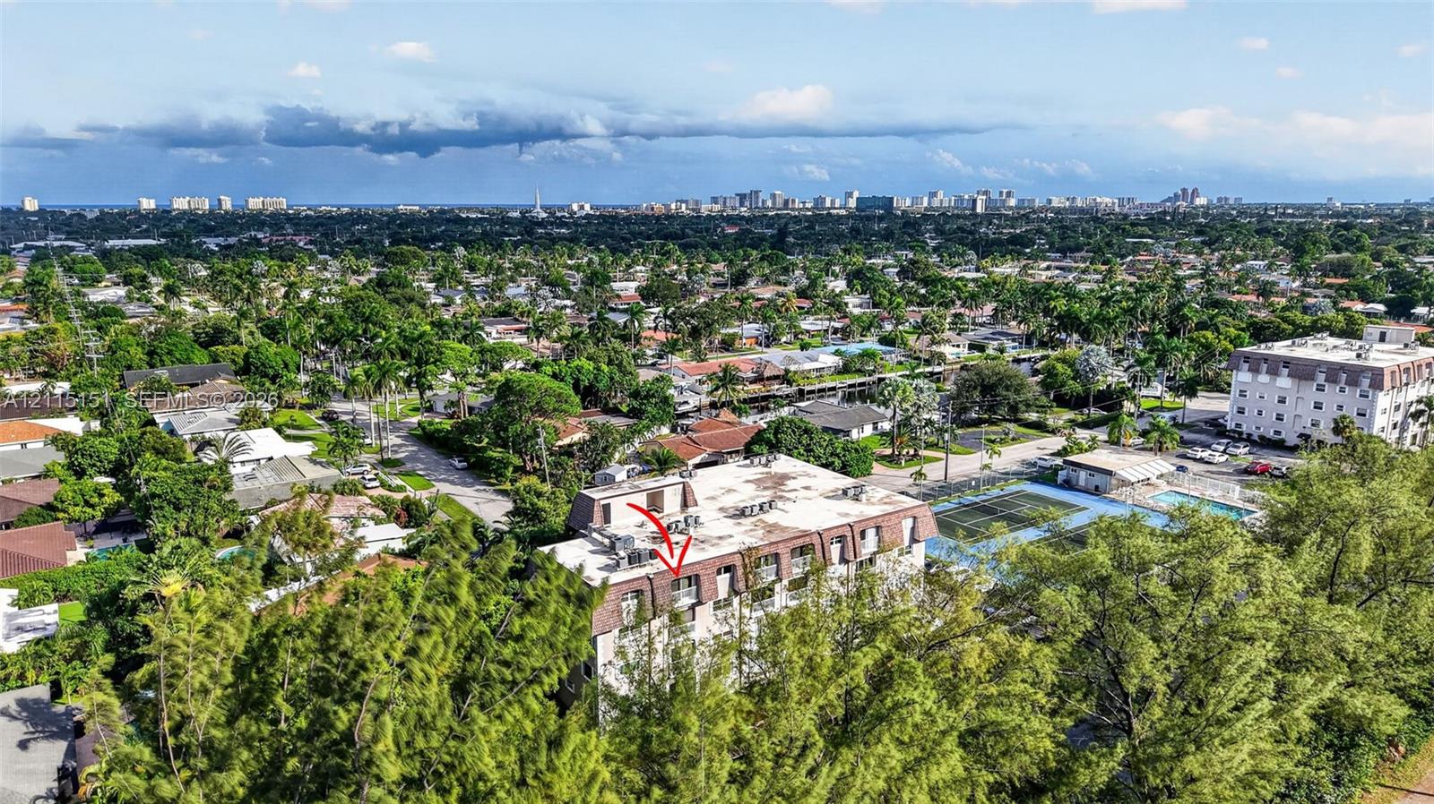 Aerial perspective of a multi-story residential building featuring a mansard roof, exterior balconies, and an on-site tennis court