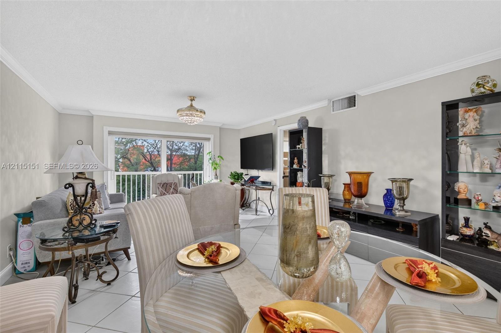 Neutral-toned interior featuring large-format diagonal tile flooring, crown molding, a crystal-style chandelier, and sliding glass doors with access to an outdoor balcony