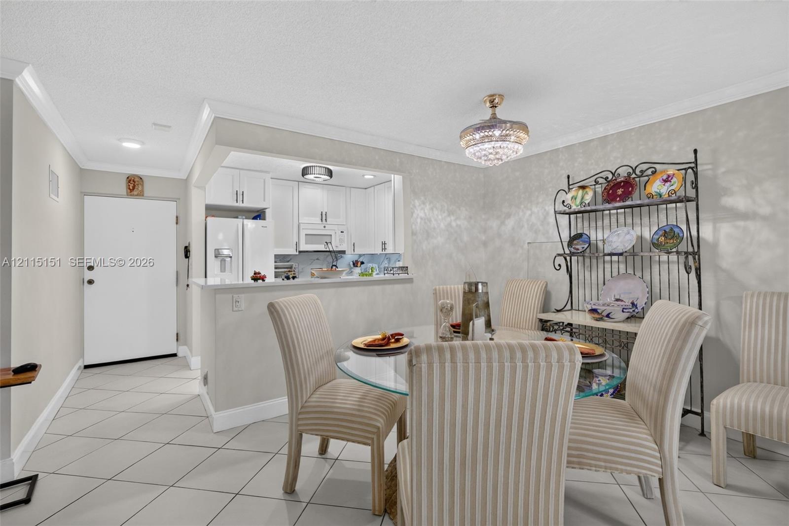 Dining area featuring crown molding, a crystal-style chandelier, and ceramic tile flooring, with a pass-through opening to a kitchen equipped with white cabinetry