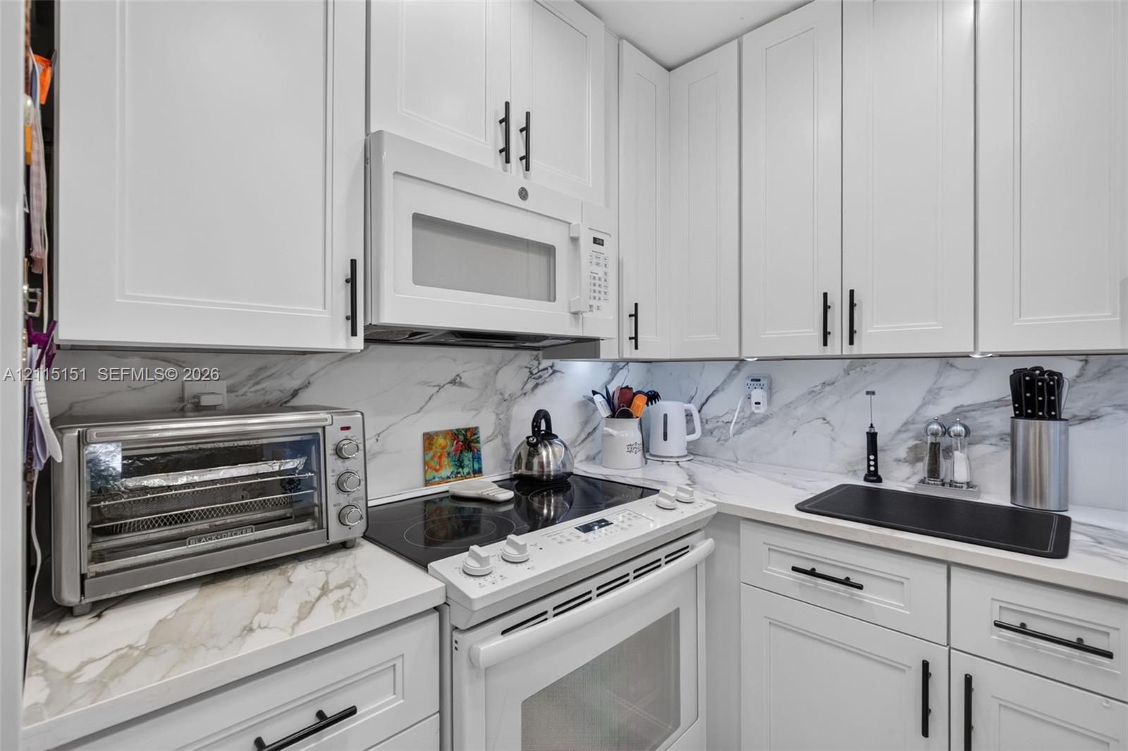 White shaker-style cabinetry with matte black hardware, stone-patterned backsplash, and matching stone-patterned countertops White shaker-style cabinetry with matte black hardware, stone-patterned backsplash, and matching stone-patterned countertops