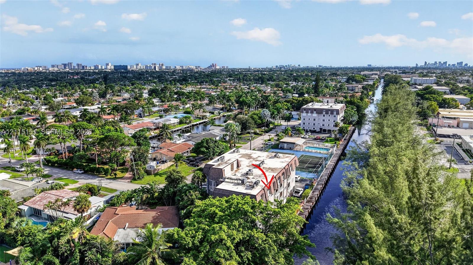 Aerial perspective featuring a multi-story residential building with water frontage, a private swimming pool, and dedicated tennis courts