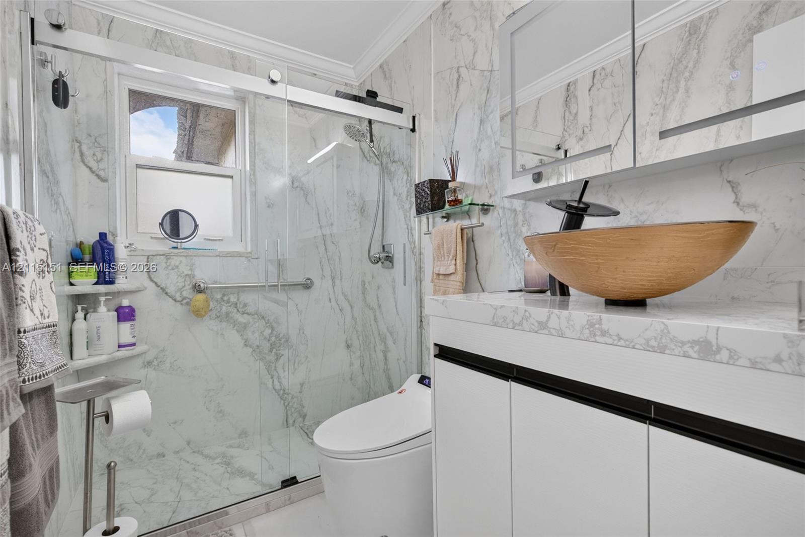 Bathroom featuring full-height stone-finish wall tile, frameless glass shower enclosure, vanity with stone-finish countertop, vessel sink with matte black faucet, and built-in medicine cabinet