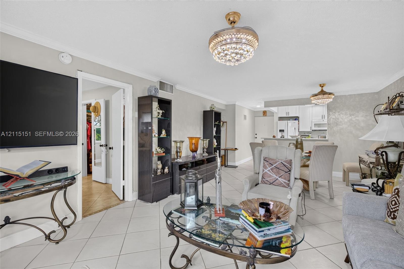 Open-concept interior featuring oversized tile flooring, crown molding, dual crystal-accented chandelier ceiling fans, and textured wall finish