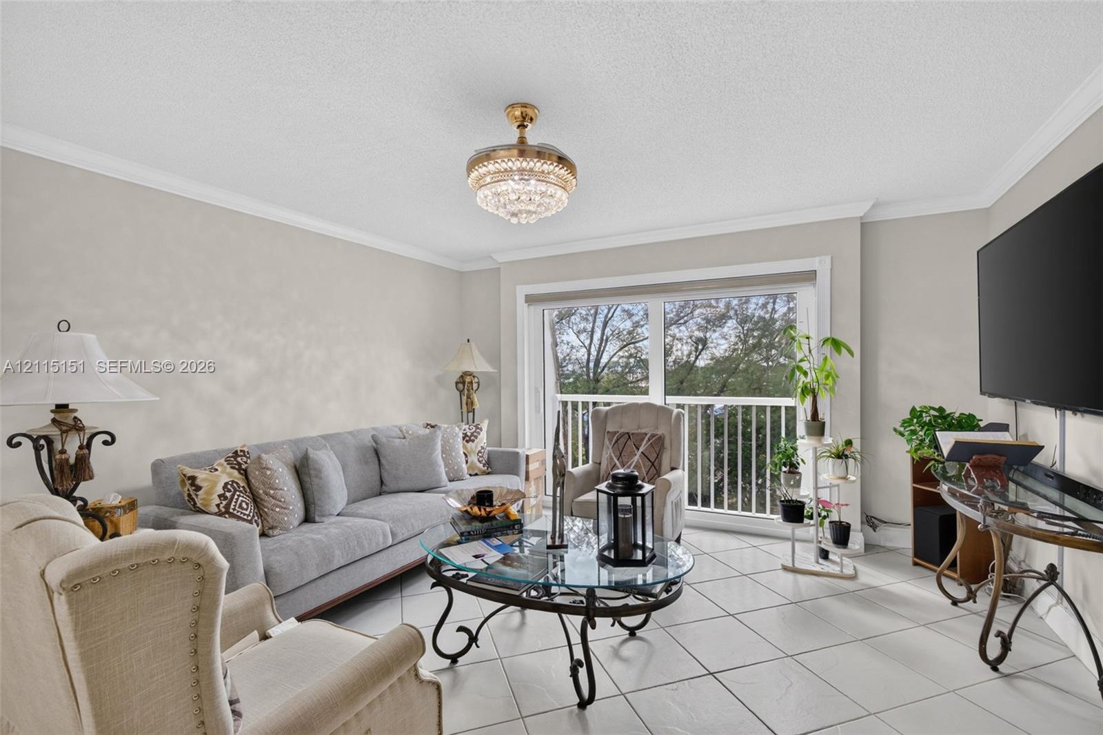 Living area featuring tile flooring, crown molding, a crystal-accented chandelier, and a sliding glass door with a balcony railing