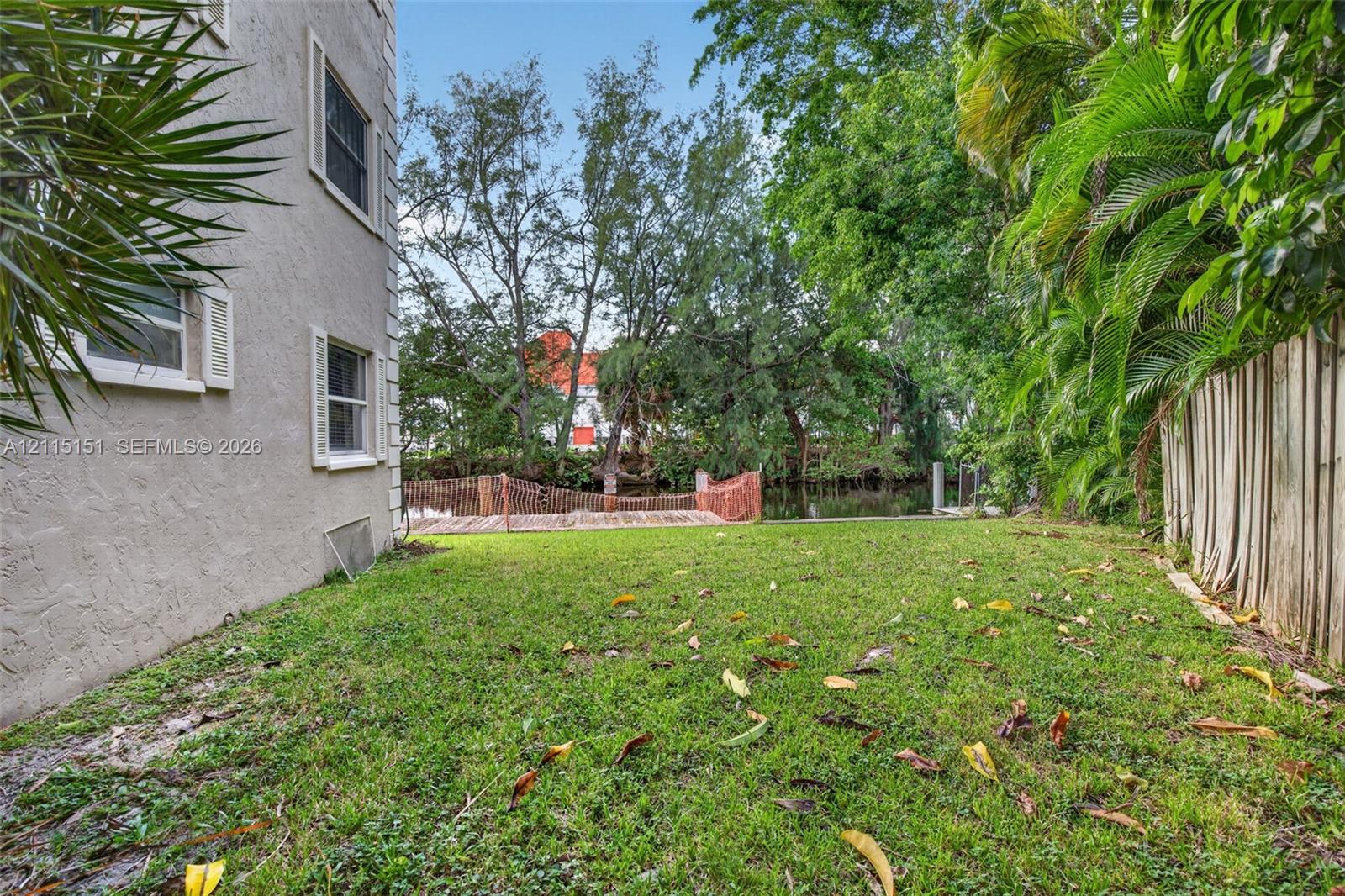 Stucco exterior, expansive lawn, mature foliage, wooden dock, and waterfront bulkhead