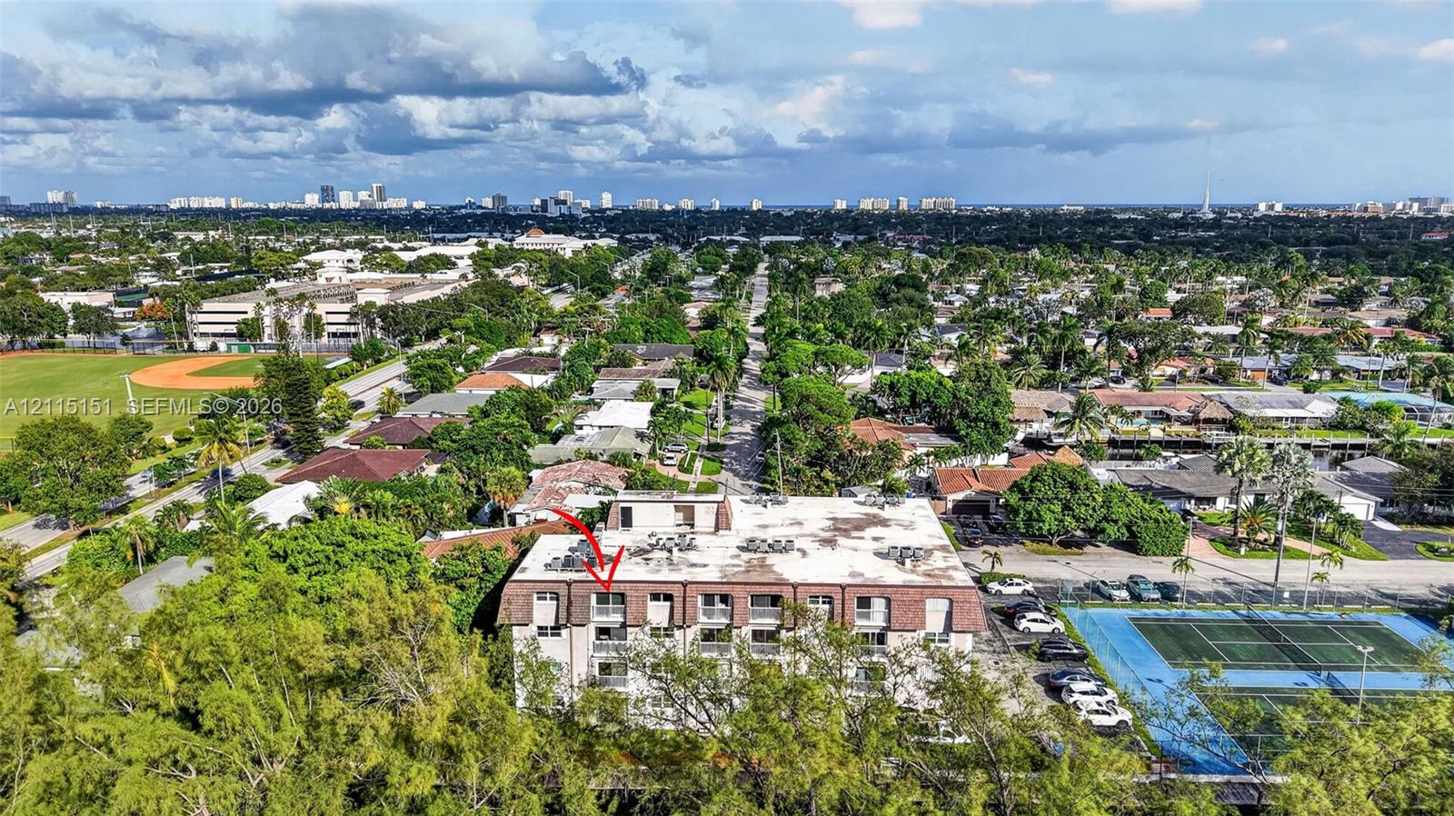 Aerial perspective of a multi-story residential building featuring private balconies, a mansard-style roof, and exterior parking