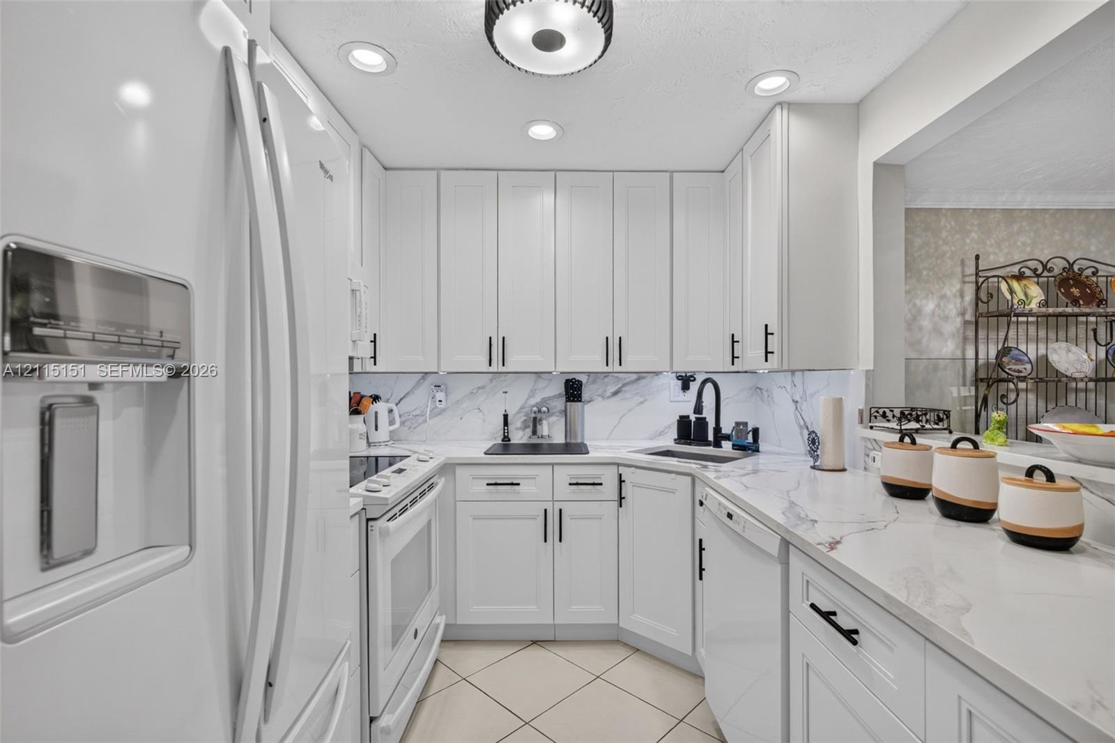 Kitchen featuring white shaker-style cabinetry, stone-finish countertops, full-height stone backsplash, matte black hardware, and recessed lighting Kitchen featuring white shaker-style cabinetry, stone-finish countertops, full-height stone backsplash, matte black hardware, and recessed lighting