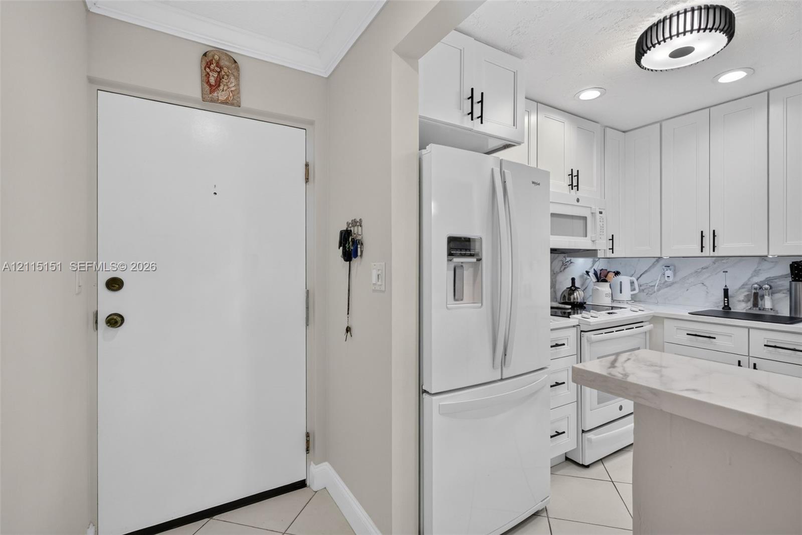 Kitchen featuring white shaker-style cabinetry, matte black hardware, stone-finish countertops, tile flooring, and integrated white appliances Kitchen featuring white shaker-style cabinetry, matte black hardware, stone-finish countertops, tile flooring, and integrated white appliances