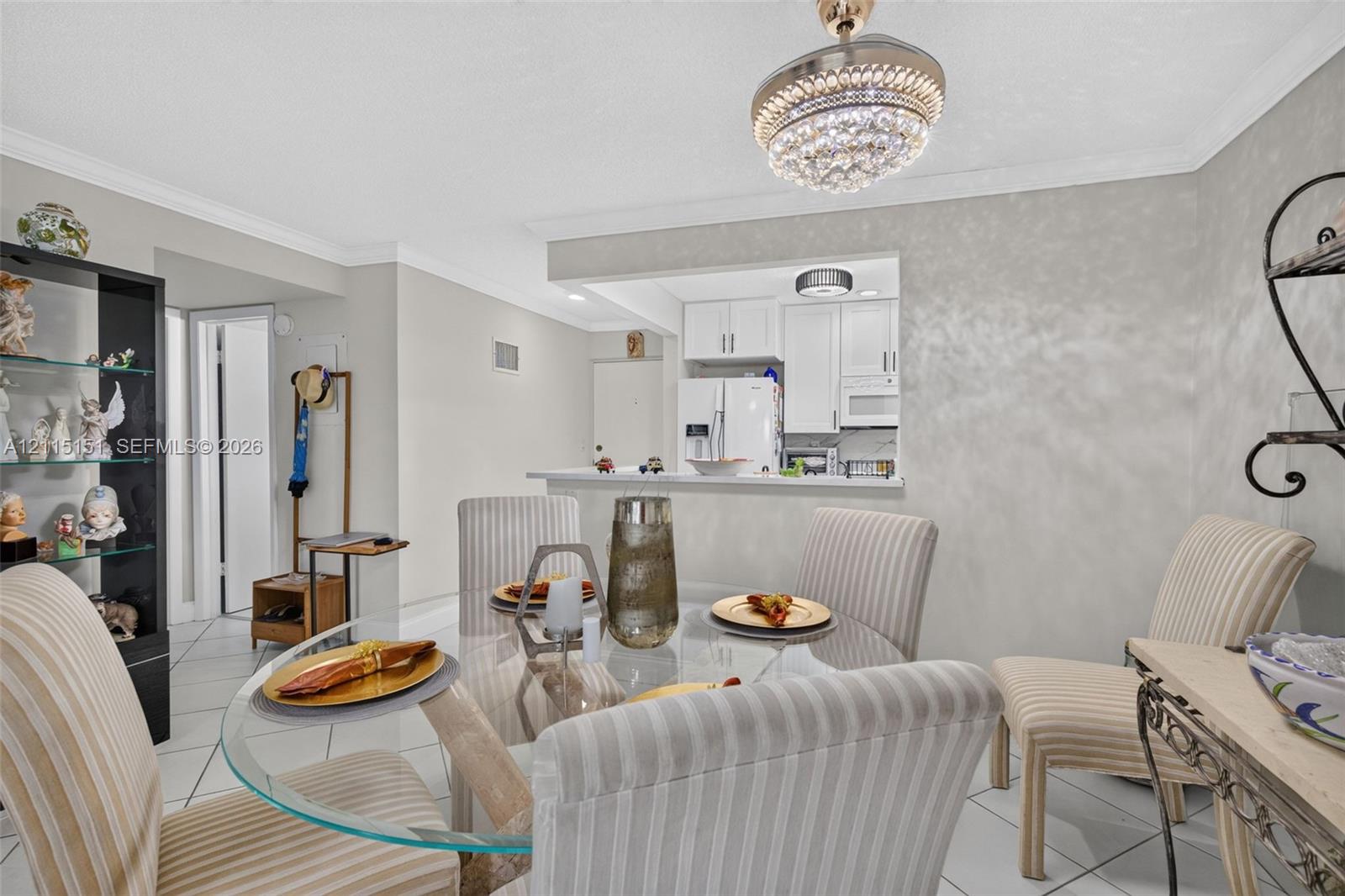 Open concept floor plan featuring a kitchen pass-through window with a breakfast bar, white cabinetry, tile flooring, and a crystal-accented ceiling light fixture