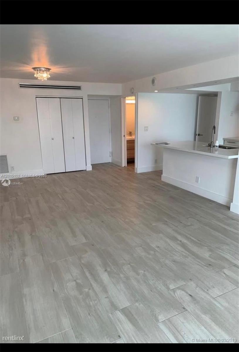 Interior space featuring wood-finish flooring, a kitchen breakfast bar with a stainless steel sink, recessed ceiling lighting, and built-in closet cabinetry