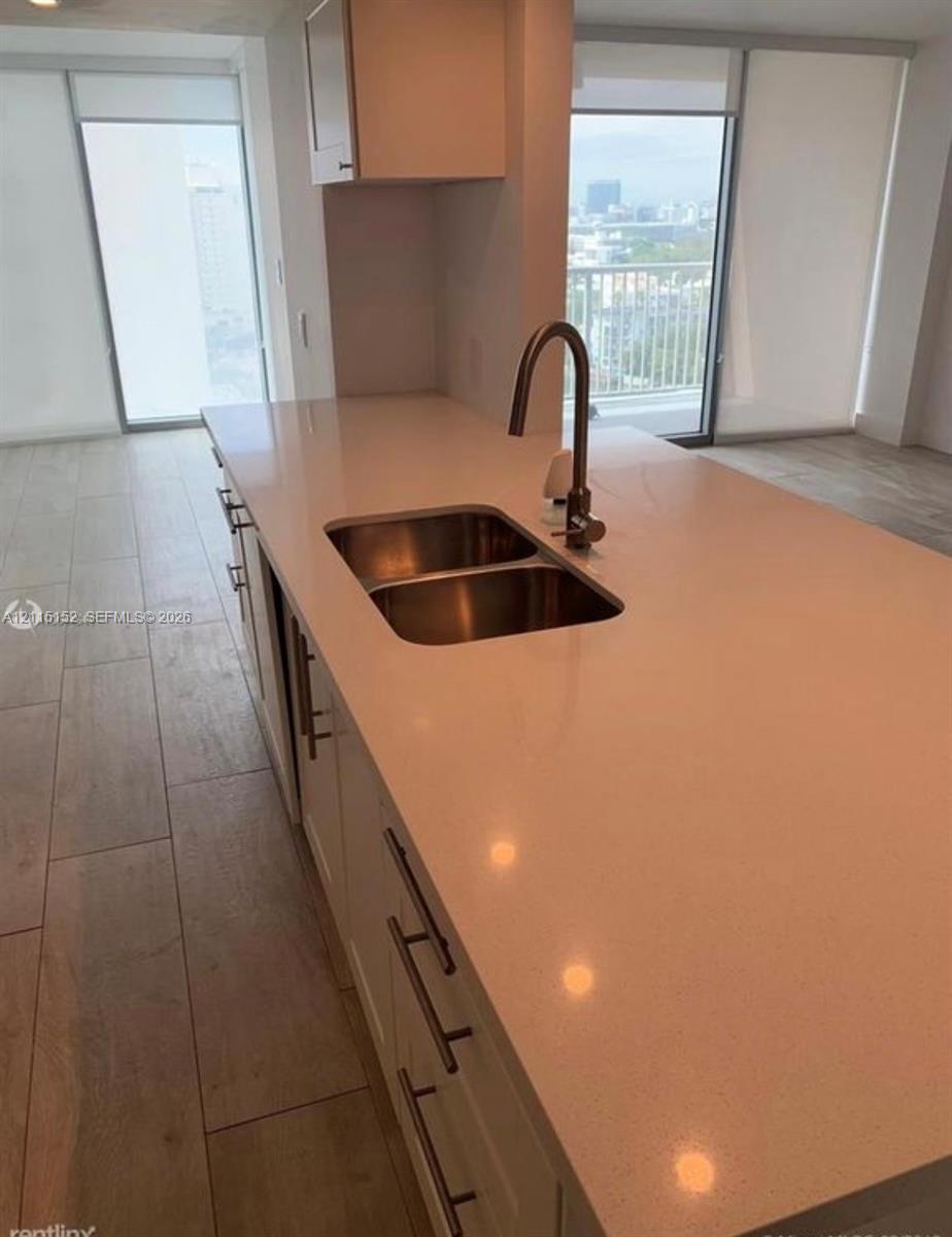 Kitchen island featuring a quartz countertop, stainless steel dual-basin undermount sink, gooseneck faucet, shaker-style cabinetry with satin nickel pulls, and wood-finish flooring