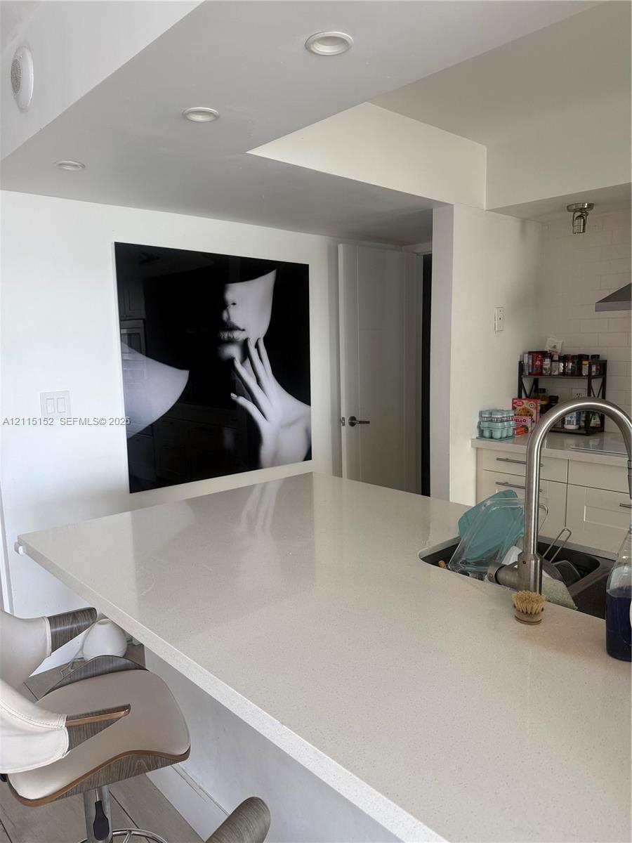 Kitchen featuring a quartz countertop island, undermount stainless steel sink, gooseneck faucet, white shaker-style cabinetry, and recessed ceiling lighting