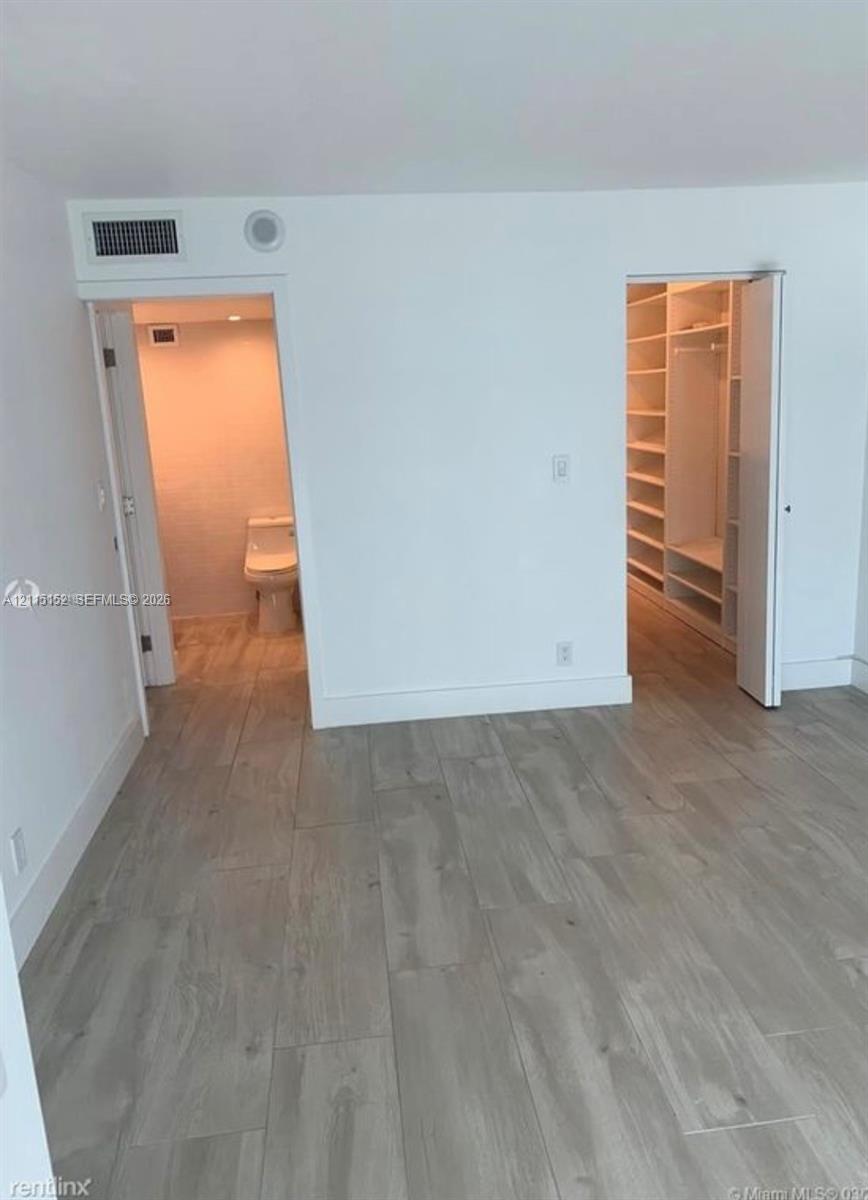 Wood-finish flooring throughout, featuring a walk-in closet with built-in shelving and an en-suite bathroom with tiled wall finishes