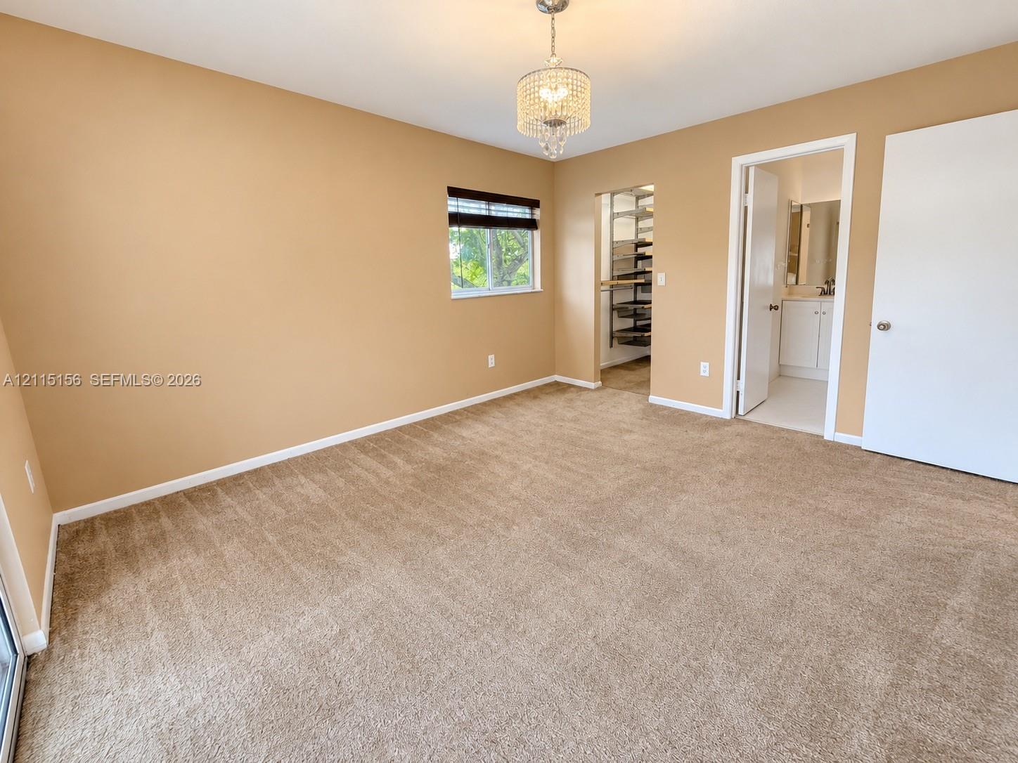 Bedroom featuring neutral carpeting, a crystal-accented chandelier, a single-pane window, a walk-in storage area with built-in shelving, and a doorway to a separate tiled space Bedroom featuring neutral carpeting, a crystal-accented chandelier, a single-pane window, a walk-in storage area with built-in shelving, and a doorway to a separate tiled space