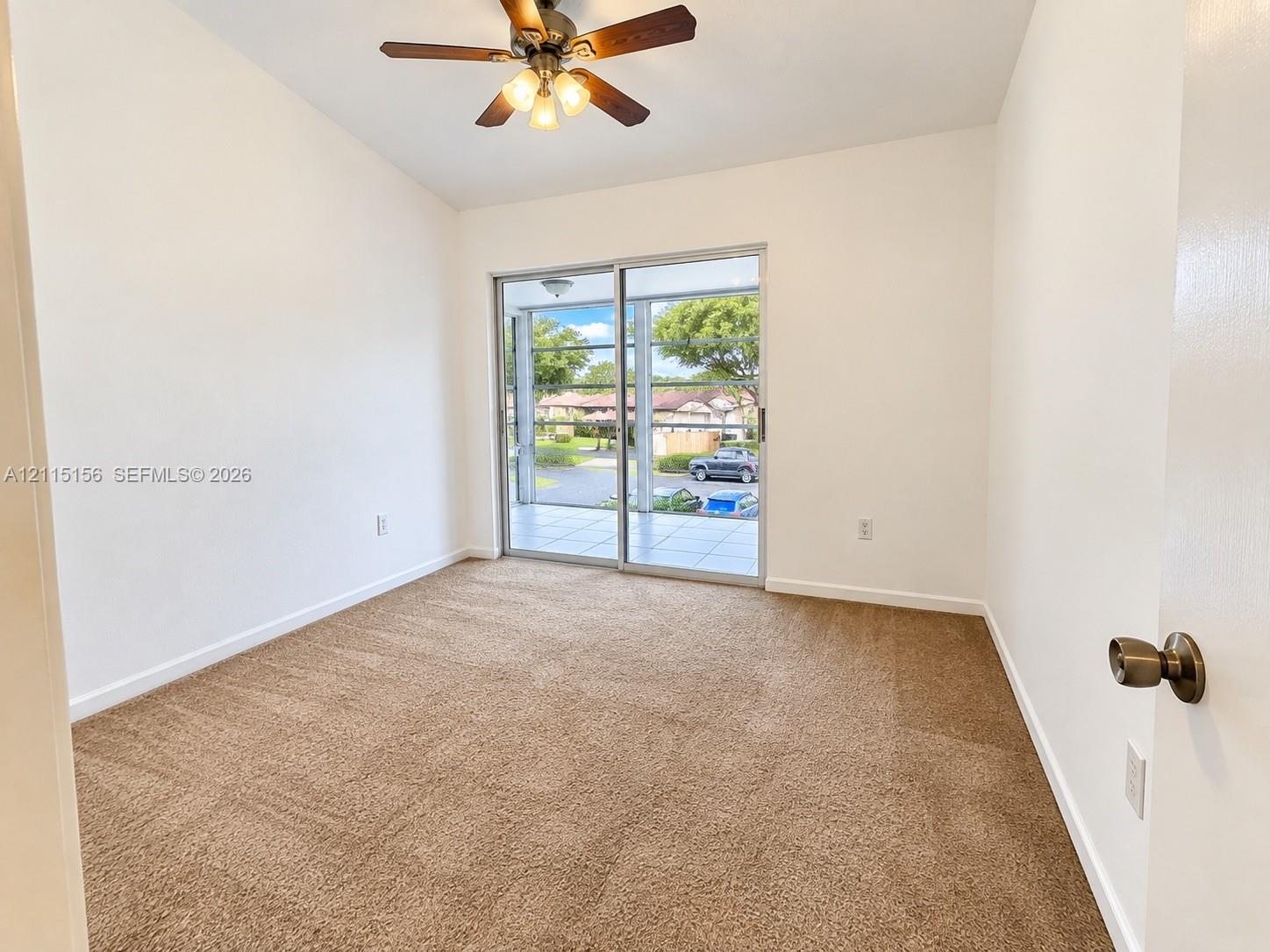 Neutral-toned wall-to-wall carpeting, vaulted ceilings, multi-blade ceiling fan with integrated lighting, and sliding glass doors with access to an exterior patio