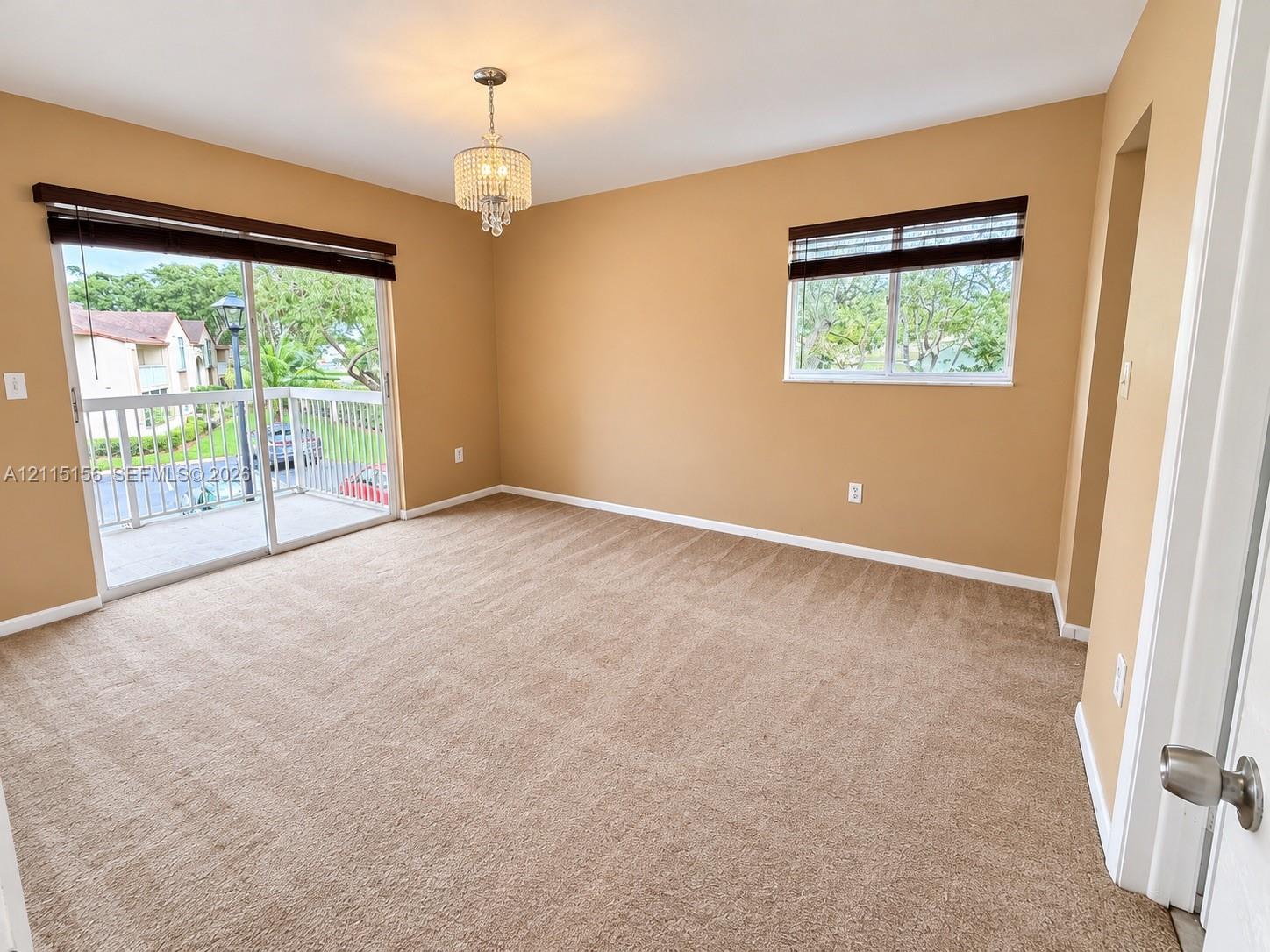 Room featuring wall-to-wall carpeting, a crystal-style chandelier, sliding glass doors to a balcony, and window treatments Room featuring wall-to-wall carpeting, a crystal-style chandelier, sliding glass doors to a balcony, and window treatments