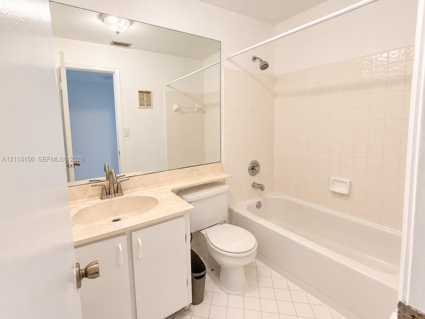 Full-width vanity with an integrated oval basin and stone-finish countertop, large wall-mounted mirror, combination tub and shower with tile surround, and diamond-pattern floor tile