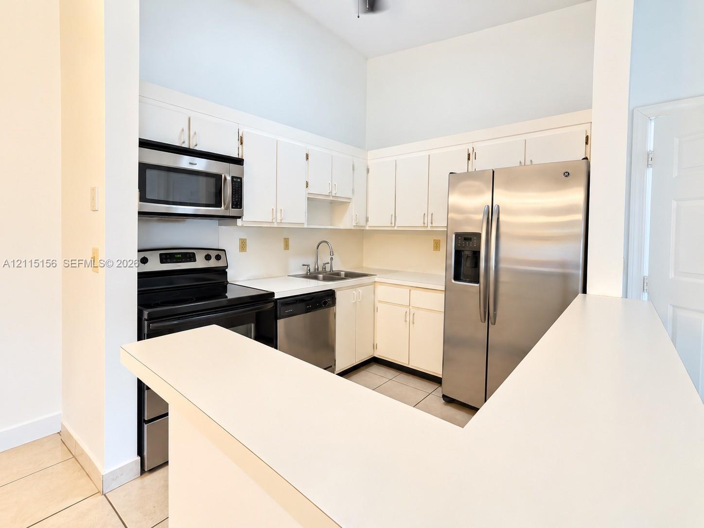 Kitchen featuring white cabinetry, solid surface countertops, stainless steel refrigerator, built-in microwave, and tile flooring Kitchen featuring white cabinetry, solid surface countertops, stainless steel refrigerator, built-in microwave, and tile flooring