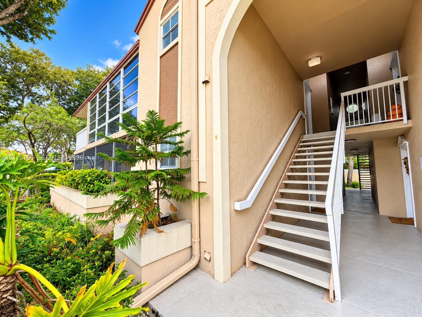 Stucco exterior featuring an arched entryway, multi-story open-air staircase, built-in concrete planter, and oversized windows