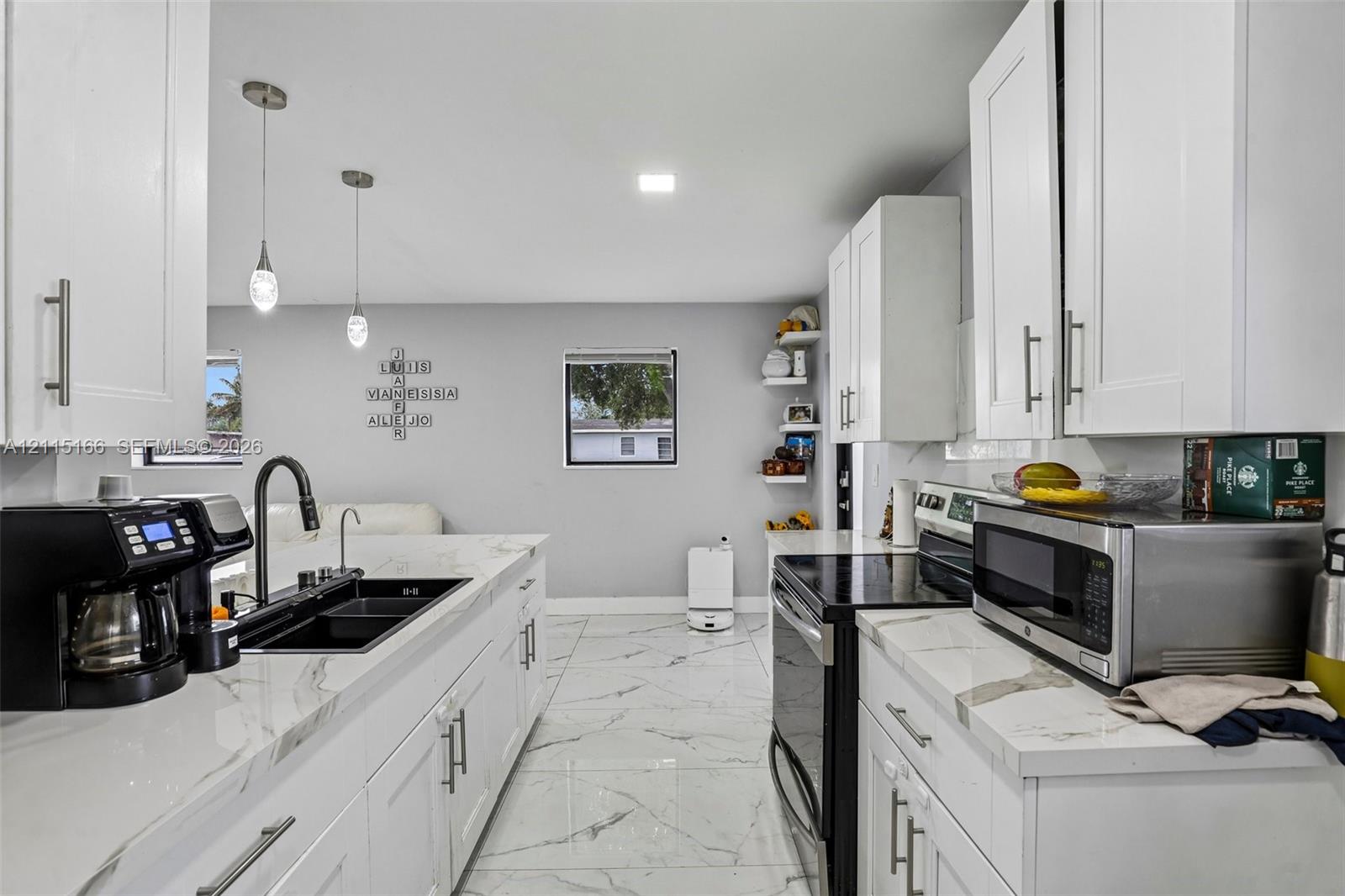 Kitchen featuring white shaker-style cabinetry, stone-finish countertops, large-format tile flooring, a dual-basin undermount sink with a matte black faucet, and pendant lighting