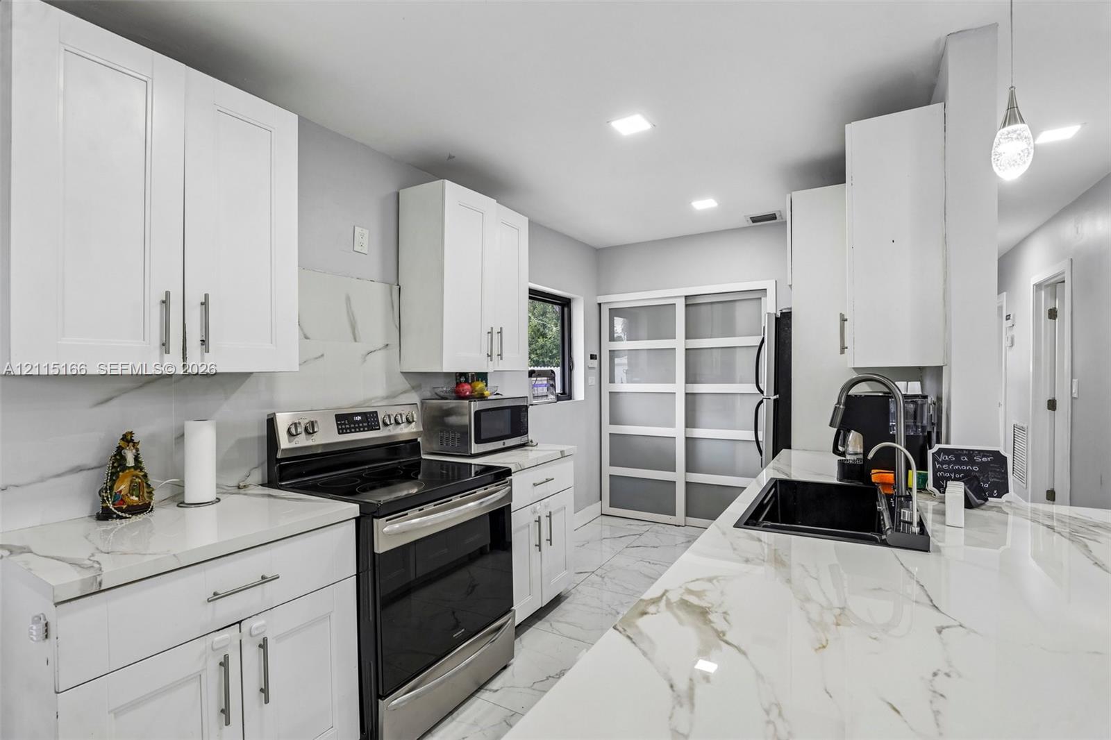 Kitchen featuring white shaker-style cabinetry, white countertops with grey veining, a stainless steel range, a black undermount sink with a pull-down faucet, and large-format tile flooring