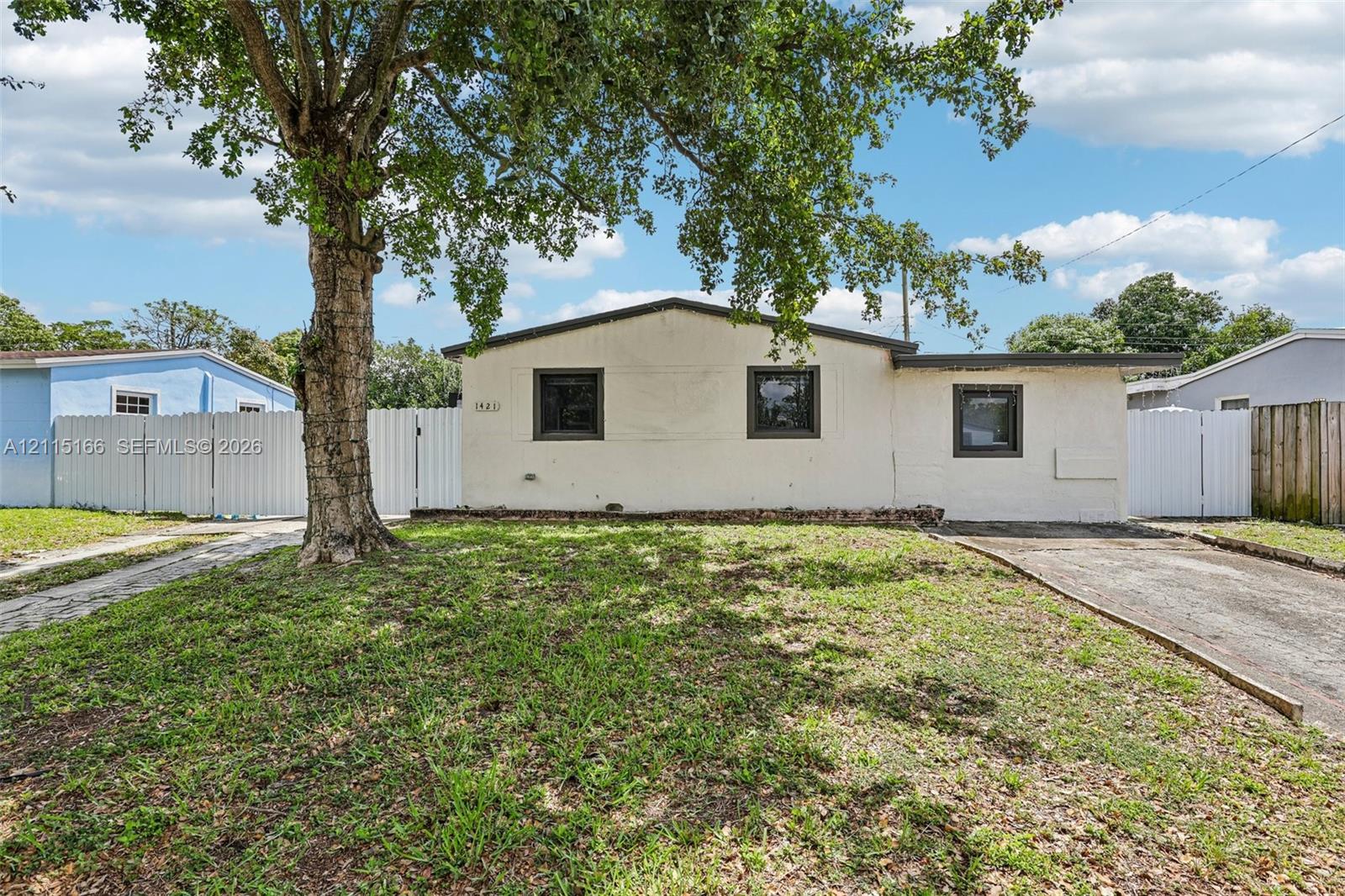 Single-story exterior with light-colored masonry, dark-framed windows, paved driveway, and white perimeter fencing