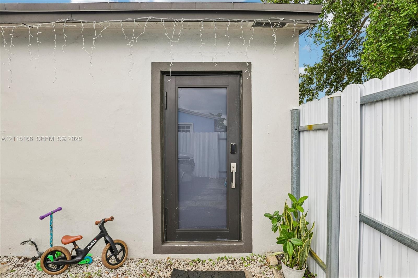Exterior access point featuring a smooth stucco finish, a full-lite glass door with a dark frame, and white corrugated metal fencing