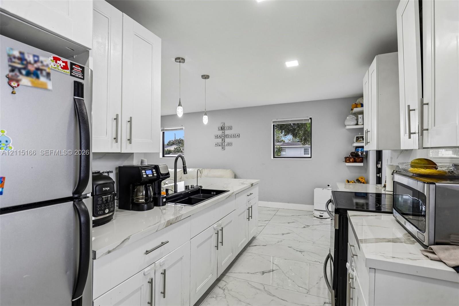 Kitchen featuring white shaker-style cabinetry, stone-patterned countertops, dual-basin undermount sink with a gooseneck faucet, large-format tile flooring, and glass pendant lighting