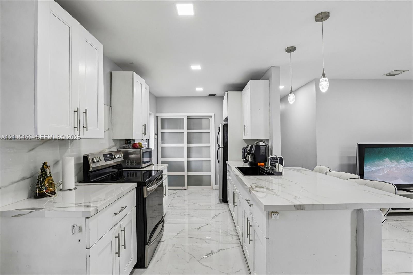 Kitchen featuring white shaker-style cabinetry, white countertops with grey veining, large-format tile flooring, recessed lighting, and dual pendant light fixtures