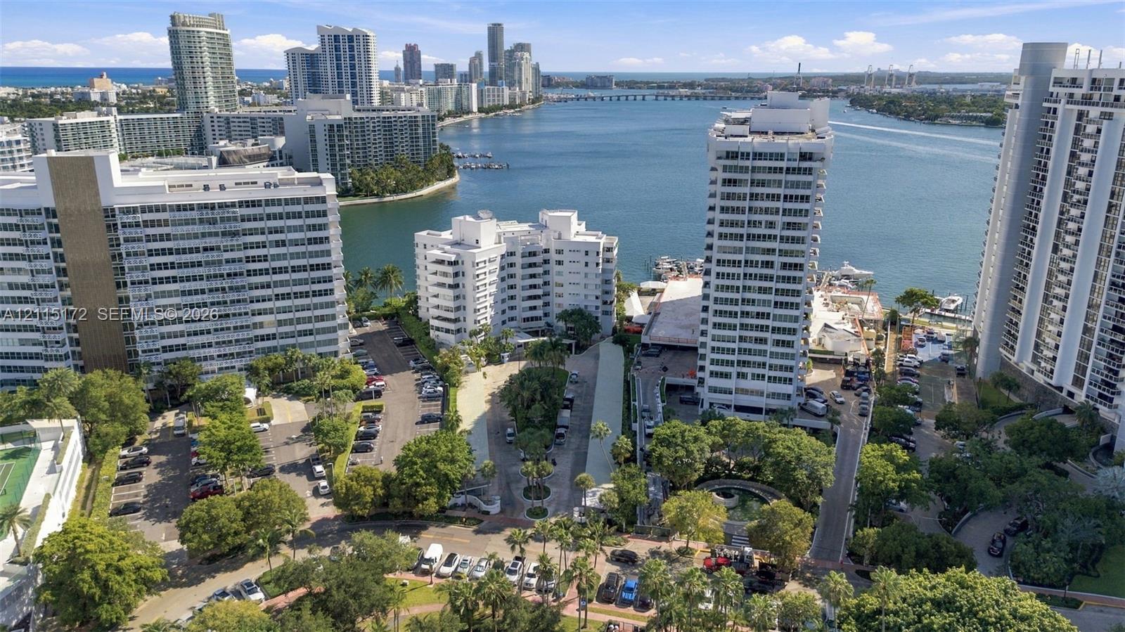 Aerial perspective of high-rise structures featuring water frontage, established landscaping, paved parking areas, and proximity to a coastal waterway
