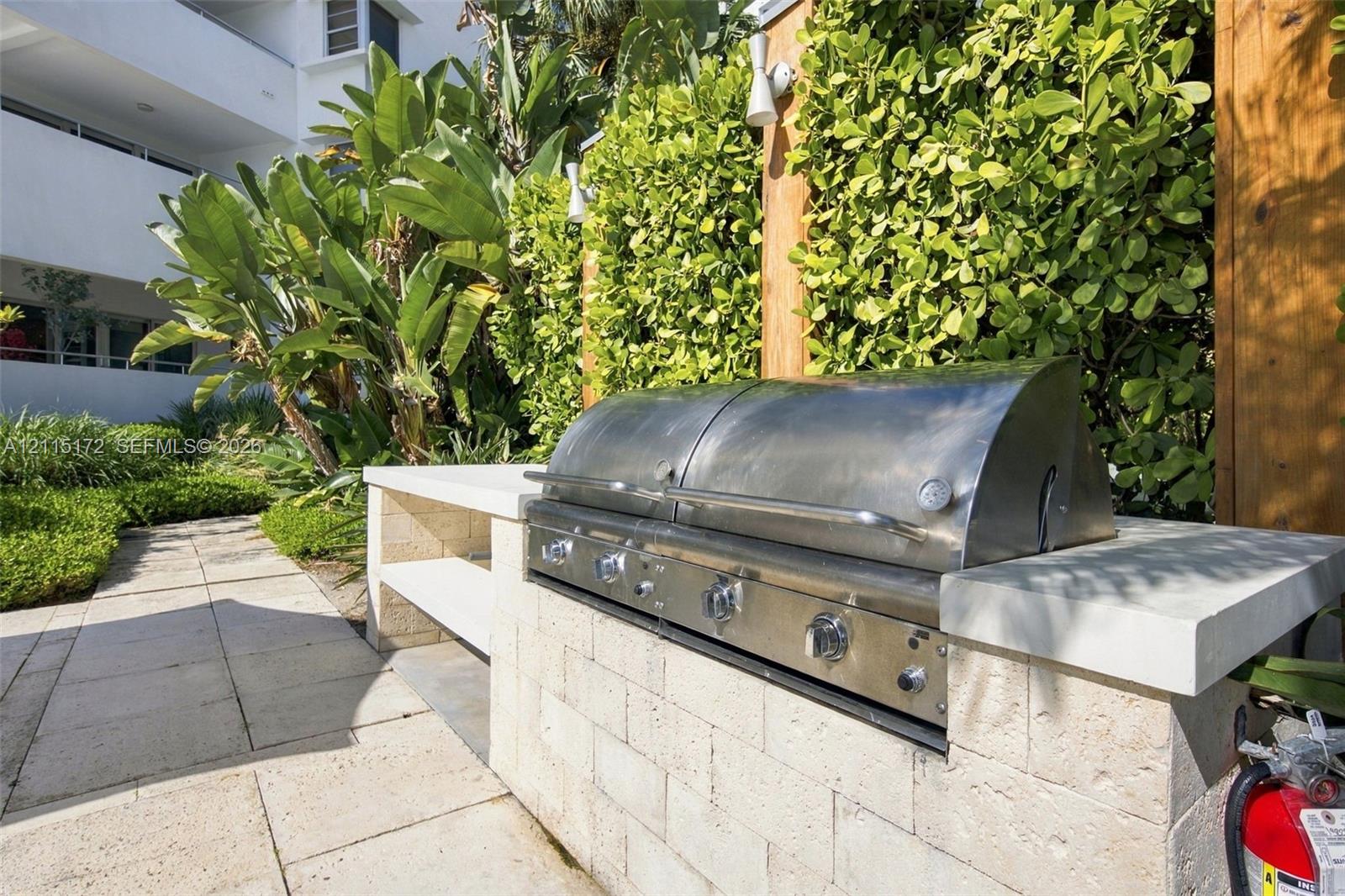 Outdoor kitchen featuring a built-in stainless steel grill, natural stone block counter, and paver hardscaping