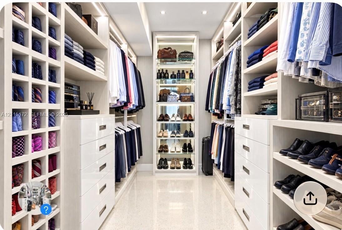 Custom dressing area featuring extensive white built-in cabinetry, floor-to-ceiling storage cubbies, integrated accent lighting, and polished stone flooring