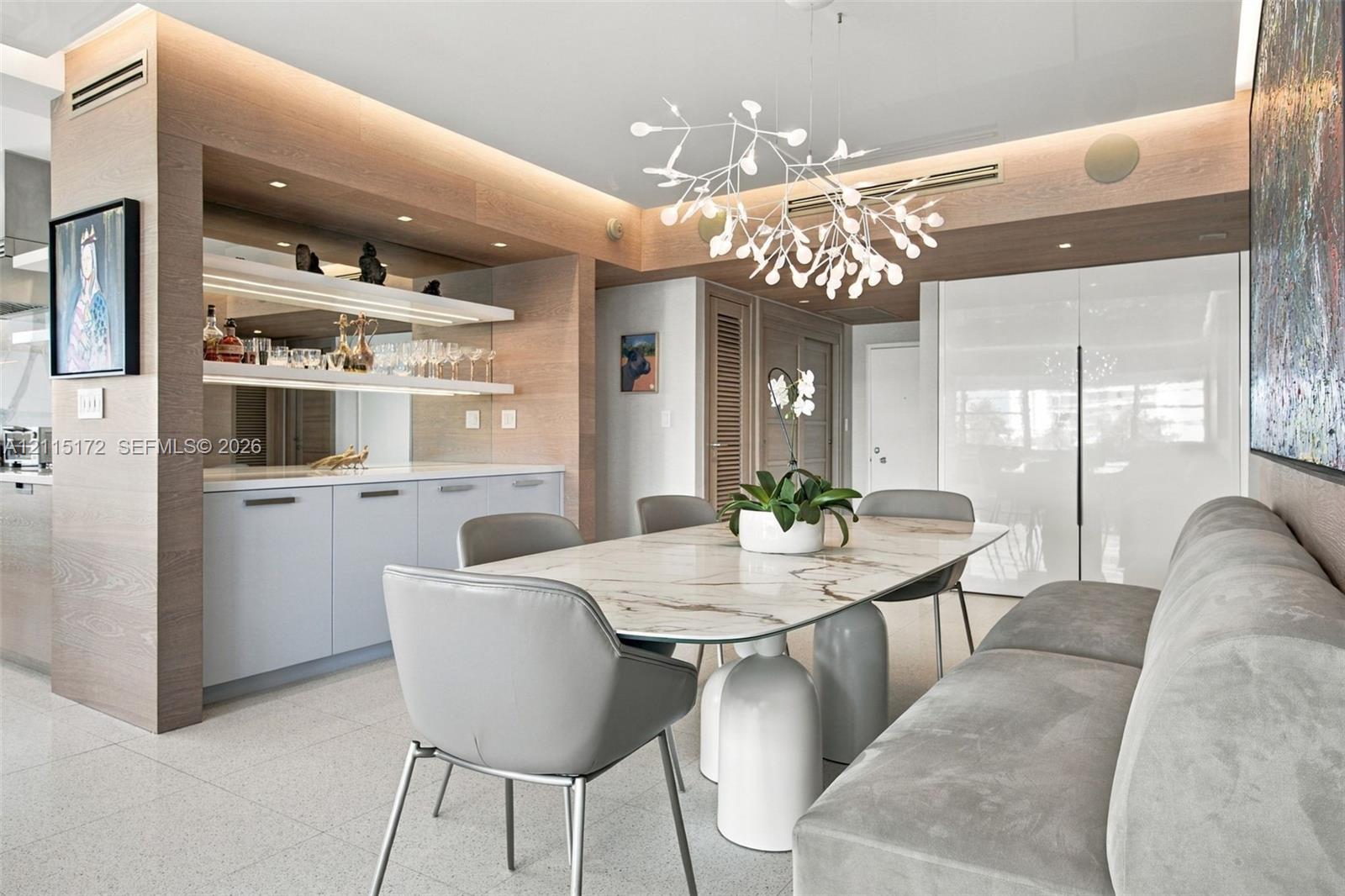 Custom built-in cabinetry with integrated lighting and stone surfacing, complemented by light-toned wood-finish wall paneling, high-gloss cabinetry, and a modern sculptural chandelier