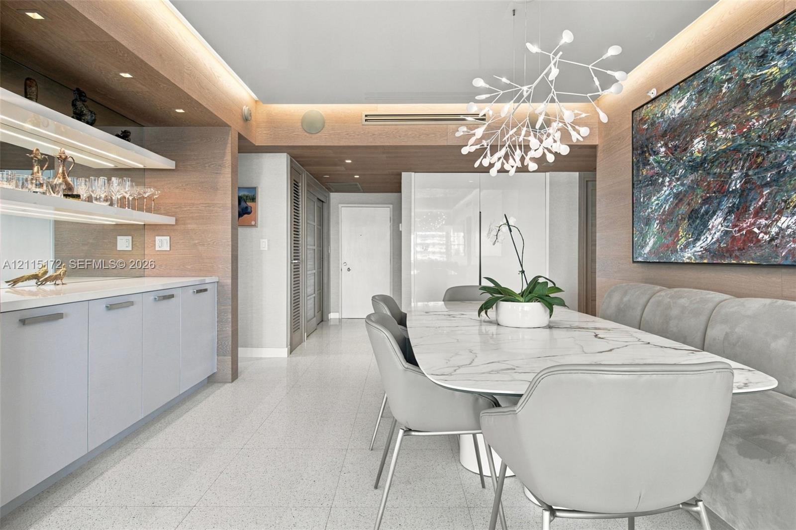 Built-in wet bar with illuminated shelving, integrated cabinetry, wood-finish wall paneling, ceiling recessed lighting, and a modern sculptural pendant fixture