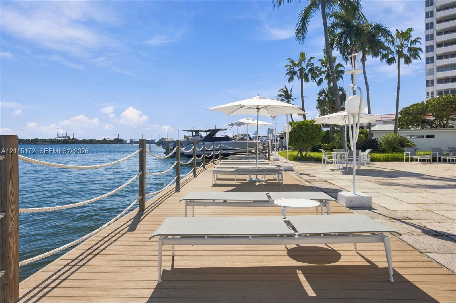 Waterfront deck featuring wood-finish decking, rope railing, stone-paved patio area, and mature palm trees
