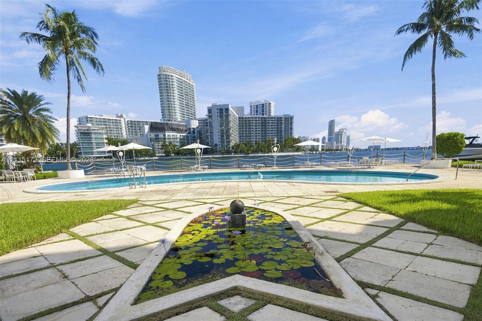 Outdoor space featuring a swimming pool, decorative pond with stone border, paved patio, manicured lawn, and perimeter fencing