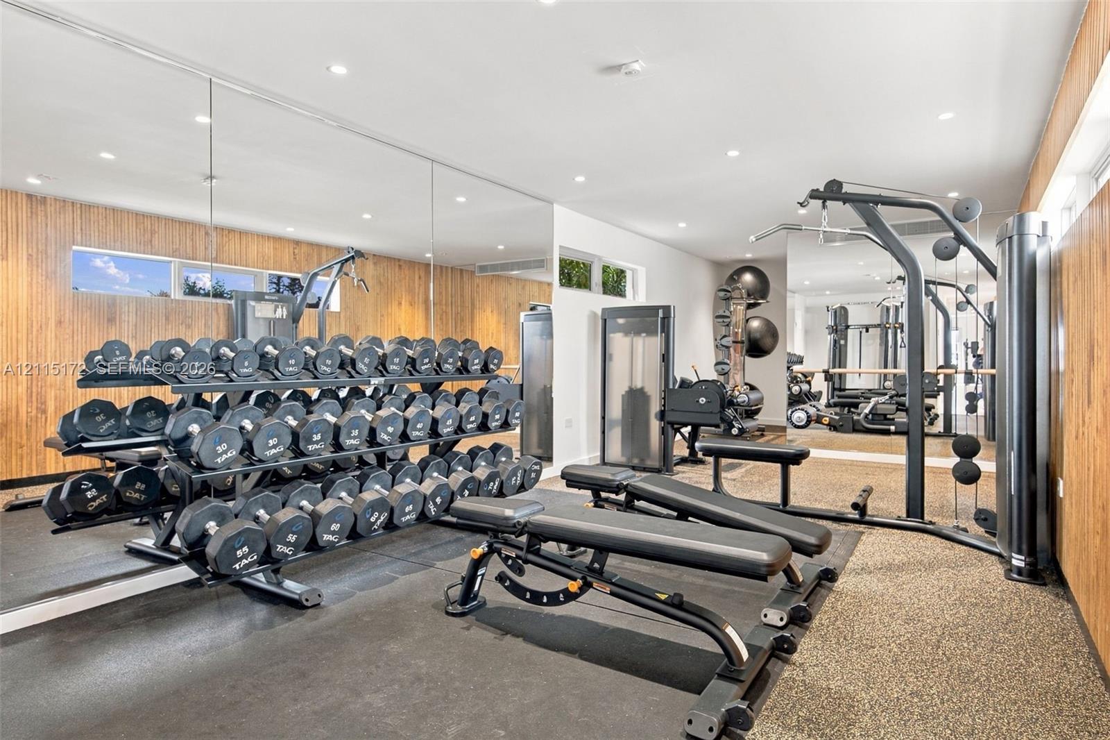 Full-wall mirrors, wood-paneled walls, recessed ceiling lighting, and textured flooring