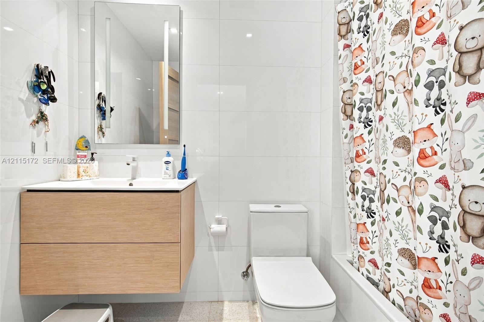 Floating vanity with wood-finish cabinetry, integrated rectangular sink, wall-mounted LED-backlit mirror, and full-height white wall tiling