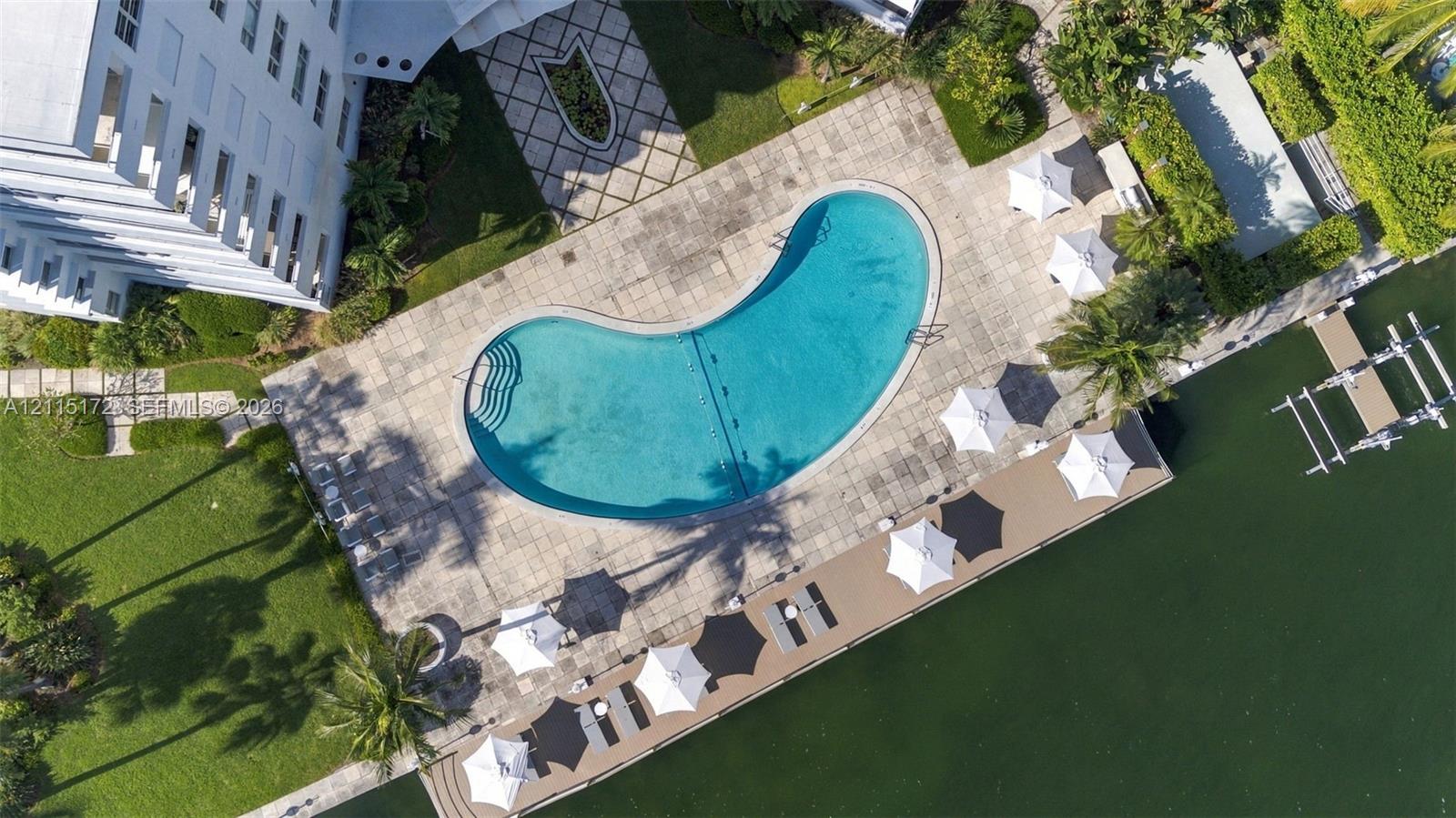 Waterfront grounds featuring a kidney-shaped swimming pool, paved stone decking, landscaped lawn areas, and a dedicated boat dock