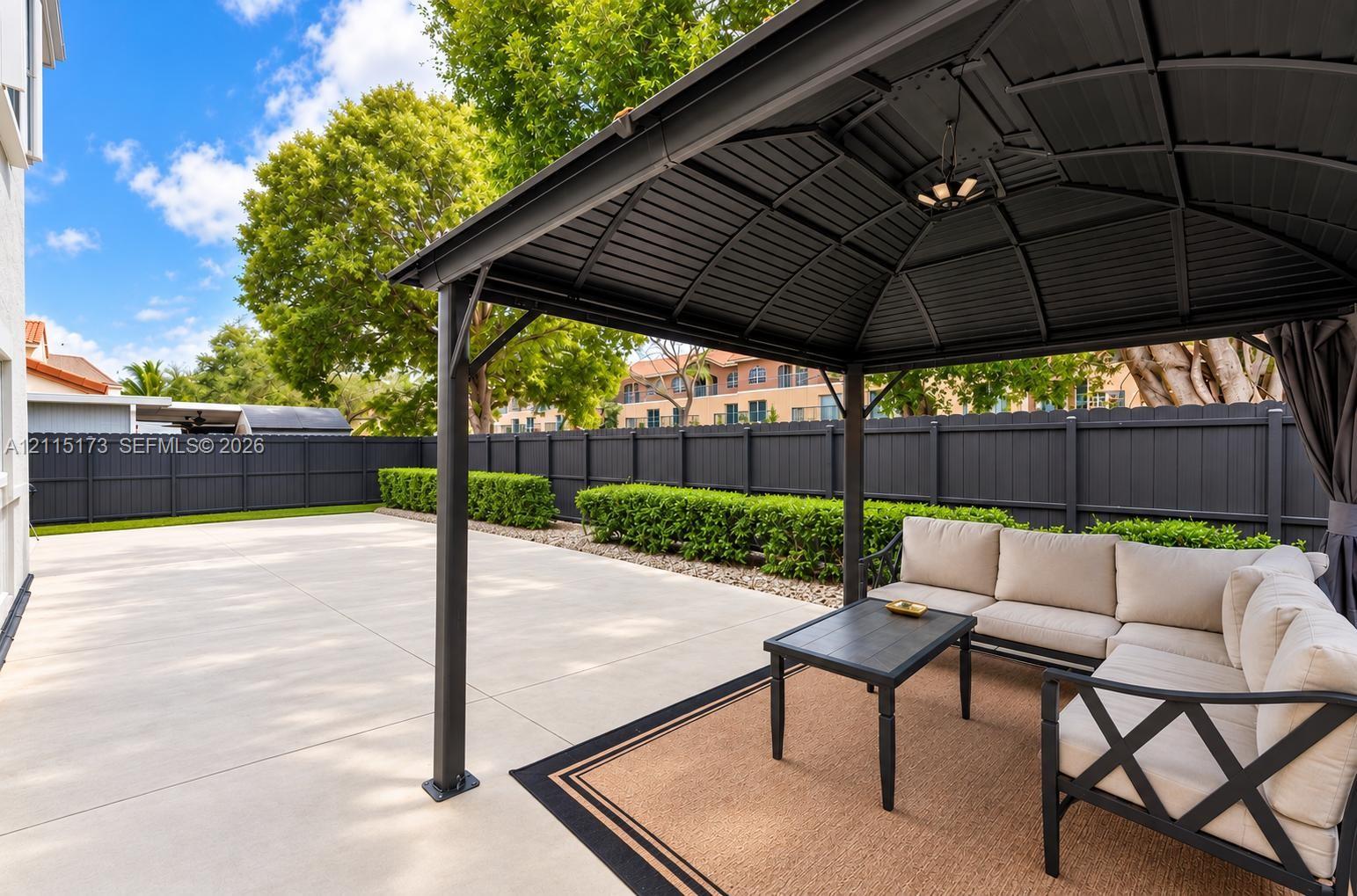 Hardscaped concrete patio featuring a metal gazebo, privacy fencing, and manicured shrubbery